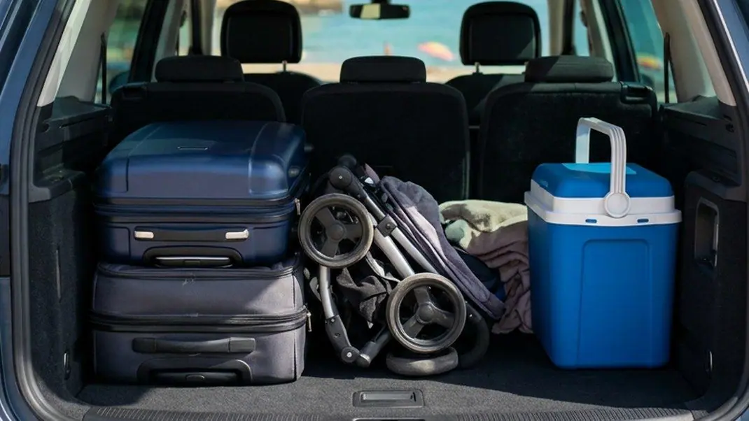 Bagageira de um carro familiar com a terceira fila rebatida, com duas malas, um carrinho de bebé dobrado e uma geleira azul, numa praia do Algarve